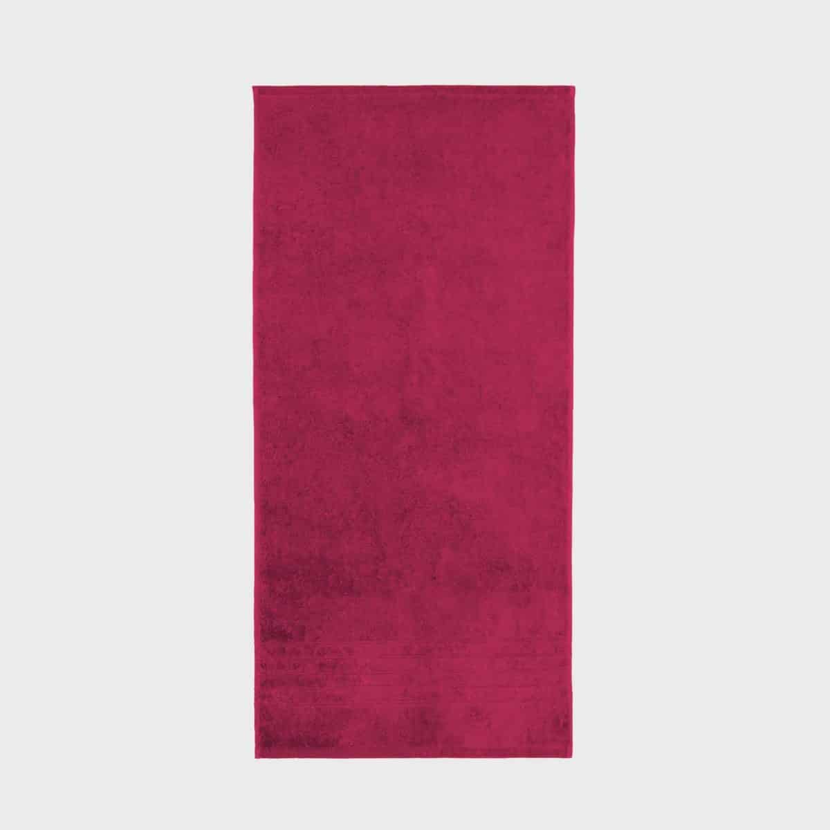 A rectangular BRILLIANT towel weighing 600 g/m² in deep red lies flat on a plain white background. The towel exudes a soft, plush texture with a luxurious density of 600 g/m² and features a subtle pattern of horizontal lines along the bottom edge.