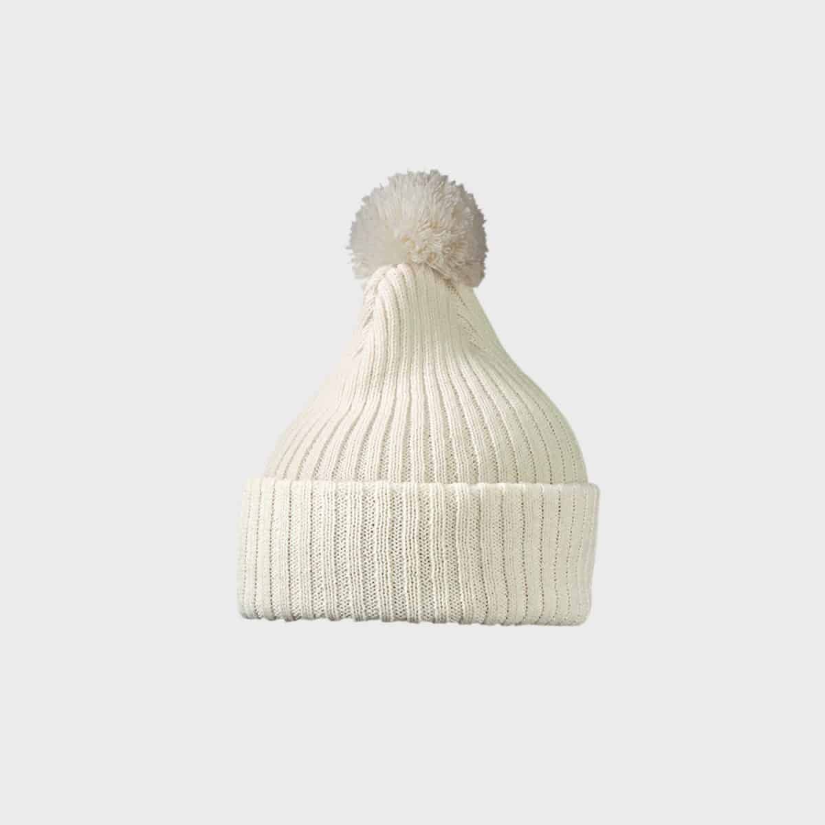 Eine cremefarbene MYRTLE BEACH Strickmütze mit Bommel mit Rippenmuster und großem Bommel oben sowie umgeschlagenem Bündchen unten vor schlichtem grauem Hintergrund.