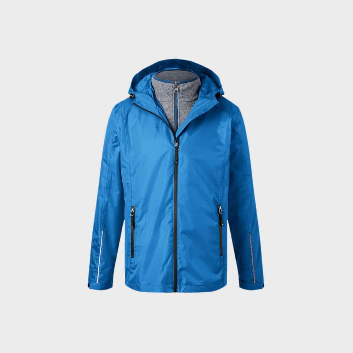Die 3-in-1-Jacke für Herren ist eine blaue Kapuzenjacke für Männer mit schwarzen Reißverschlüssen an den Vordertaschen und der Hauptöffnung. Sie verfügt über verstellbare Kordeln an der Kapuze und reflektierende Streifen in der Nähe der Manschetten. Das graue Innenfutter mit hohem Kragen ist darunter sichtbar und zeigt vielseitige Oberbekleidung für Männer.