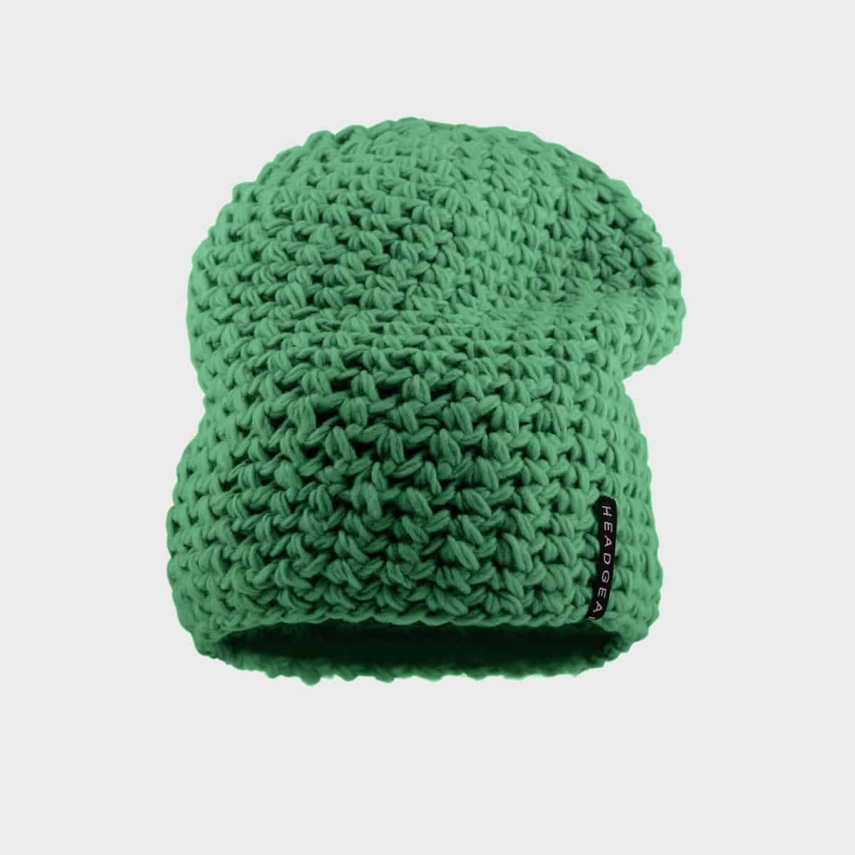 Eine grüne, grob gestrickte Beanie mit lockerer Passform. Die Beanie hat ein kleines schwarzes Etikett mit weißem Text in der Nähe der Krempe. Auf dem Etikett steht „HEADGEAR“. Der Hintergrund ist weiß, wodurch die Beanie hervorsticht.