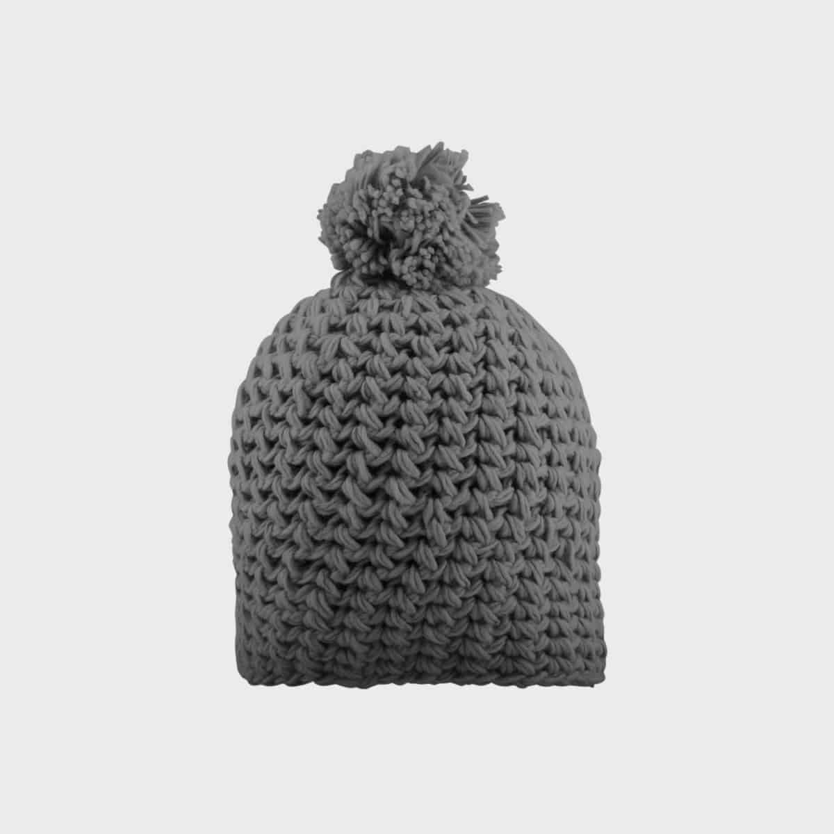 Eine graue Strickmütze mit dicker, grober Webart und einem großen Bommel obenauf ist zentriert vor einem schlichten weißen Hintergrund angebracht.